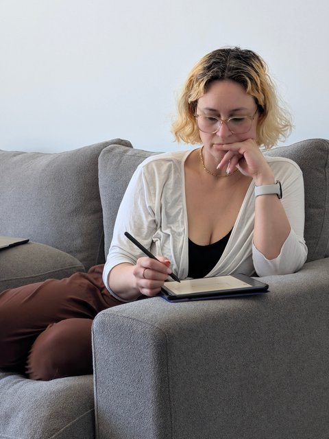 Lynn Baxter sketching on a tablet from the corner of a grey couch
